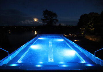 Infinitypool på natten. Upplyst med blå lampor och stjärnklar himmel.